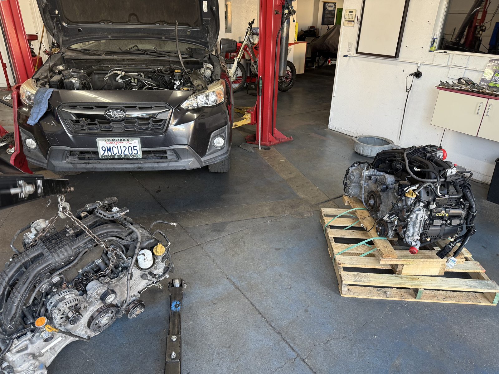 Engine swap in progress, with the old engine on a pallet beside the car